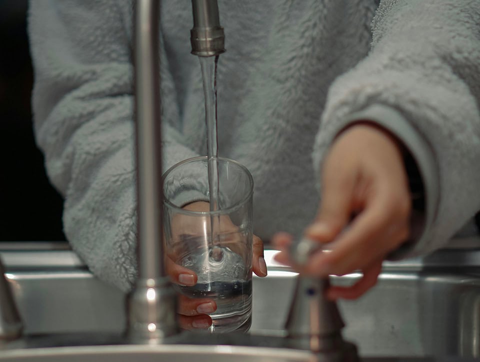 Mani che tengono un bicchiere mentre viene riempito di acqua del rubinetto
